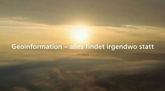 Der Bildausschnitt aus dem Imagefilm über Geoinformation zeigt die Sonne über den Wolken. Davor der Text: Geoinformation - alles findet irgendwo statt.